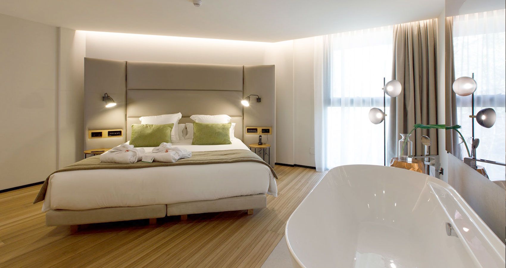 Suite Deluxe: llit king amb barnussos i banyera exempta en primer pla al costat del finestral