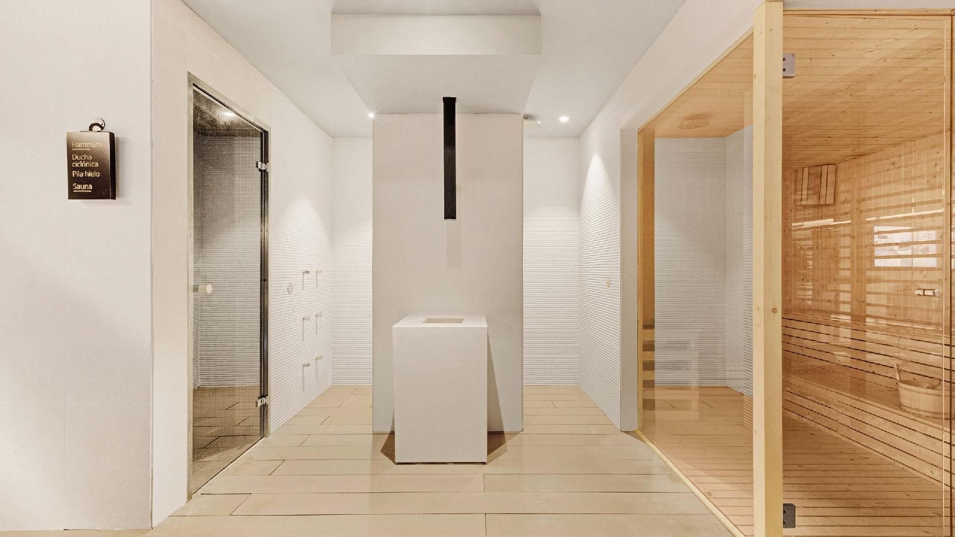 Thermalbereich mit der Hammam-Tür links, einer Dusche und der Saunakabine aus Holz mit Glaswänden rechts; ein Schild weist auf Hammam, Erlebnisdusche, Eisbrunnen und Sauna hin