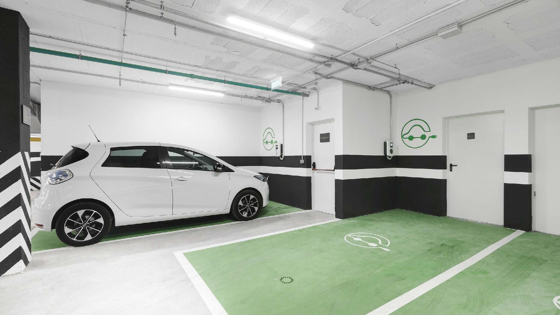 Places de parking vertes avec borne de recharge pour voiture électrique, et une voiture blanche garée