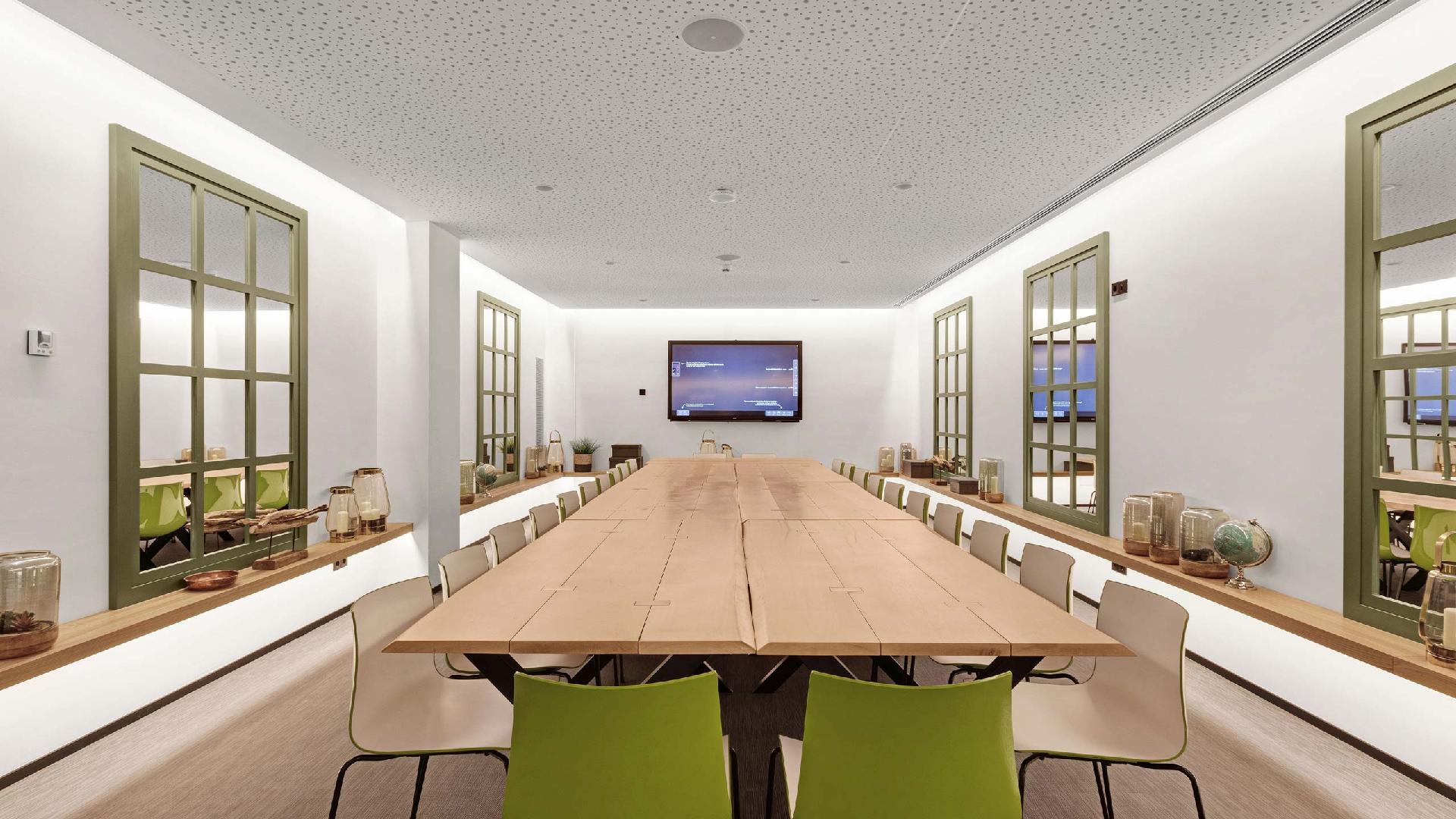 Sala alargada con una gran mesa de madera, sillas y una pantalla al fondo