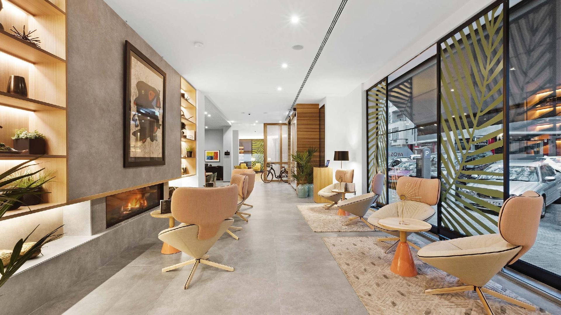 Hotel lobby with a lit fireplace, a large painting, peach-coloured armchairs and a large window with a palm-tree lattice