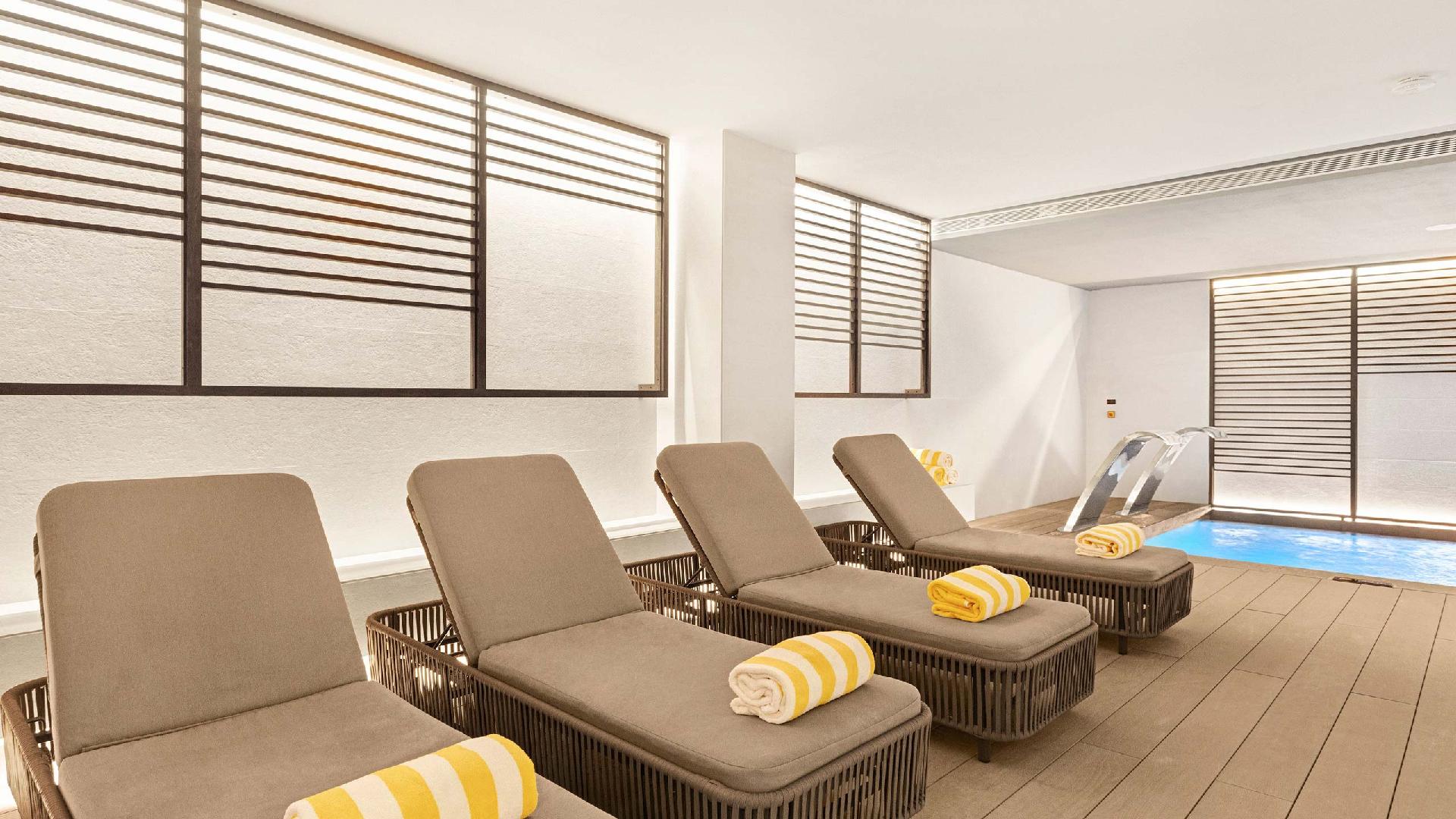 Bains de soleil marron avec serviettes jaunes près de la piscine intérieure du spa