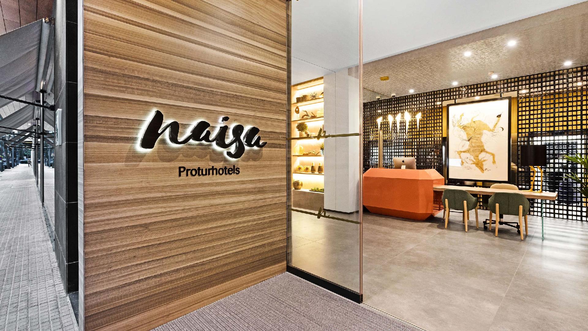 Hoteleingang mit Holzpaneel und dem Schriftzug naisa Proturhotels; im Hintergrund ein orangefarbener Empfangstresen und ein großes Gemälde