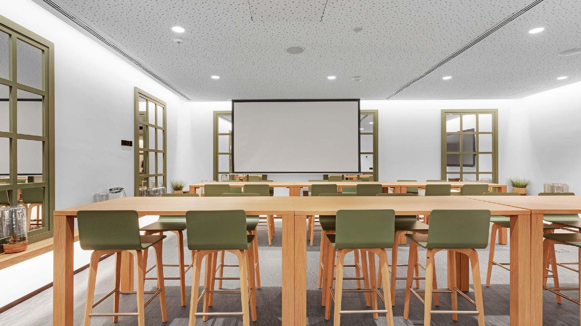 Room with high tables and green stools, and a projection screen