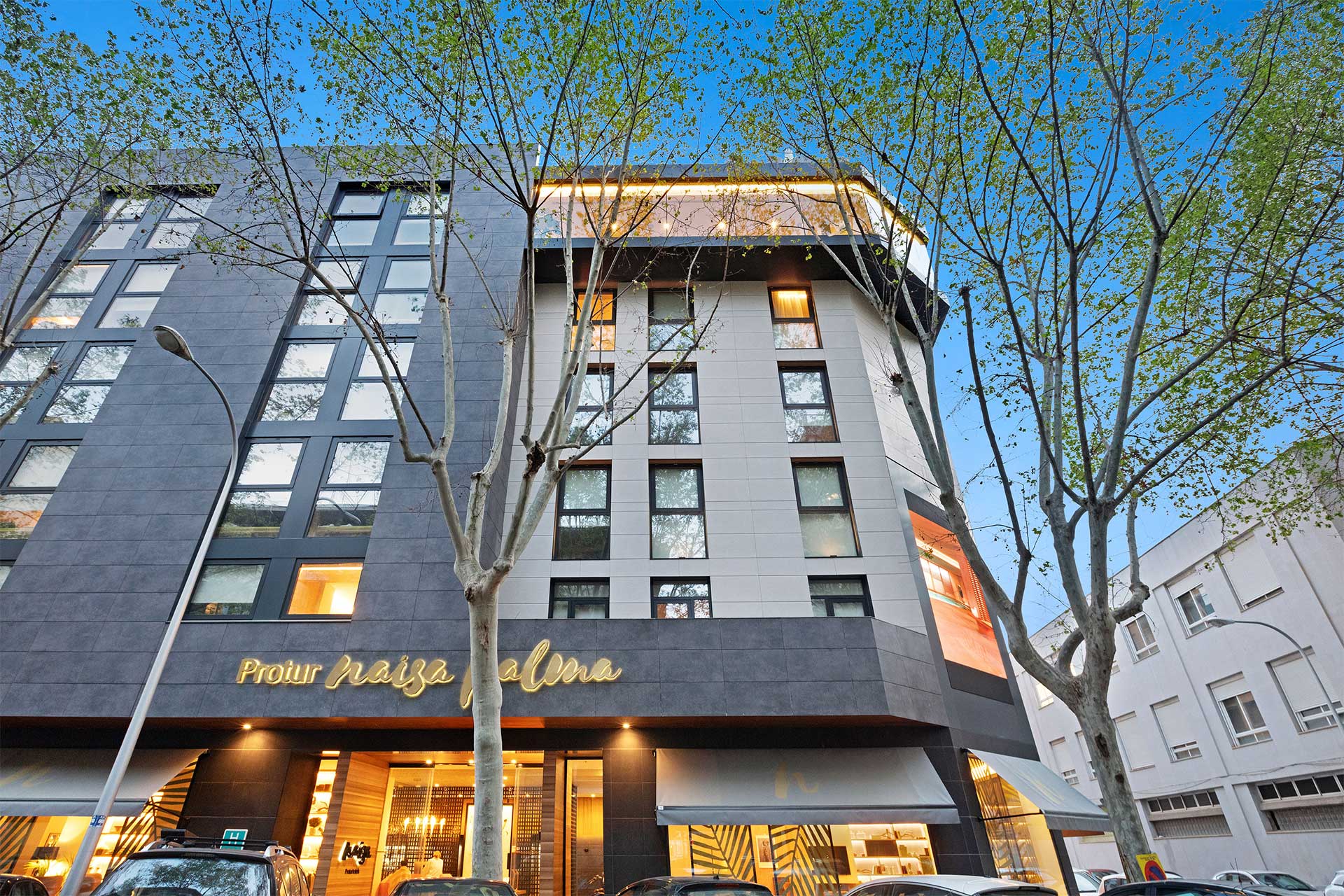 Hotelfassade in der Abenddämmerung, mit beleuchtetem Schriftzug Protur Naisa Palma und dem warmen Foyer auf Straßenebene
